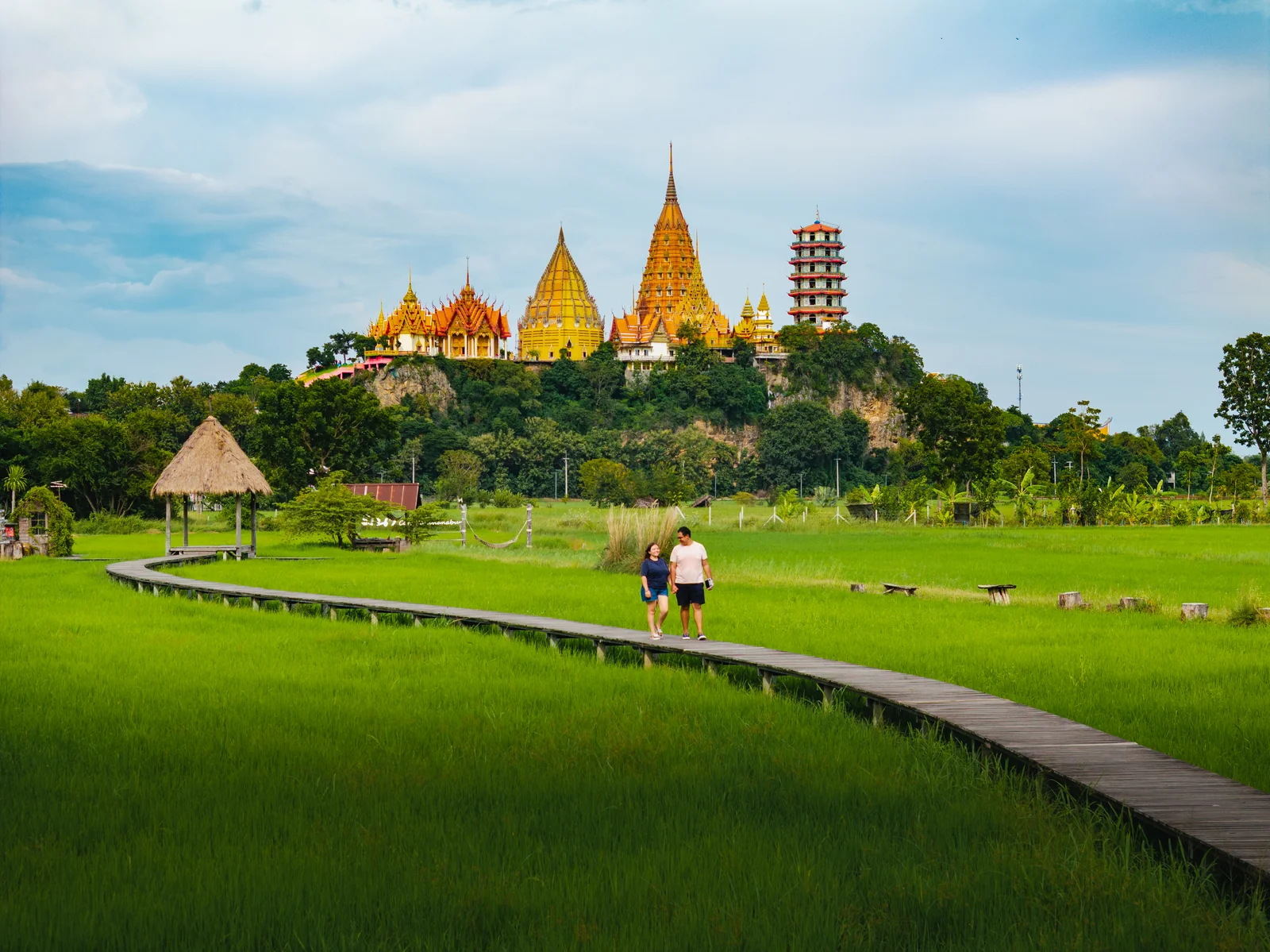 Pao y Andrew recorriendo juntos un arrozal de Kanchanaburi, con un templo al fondo