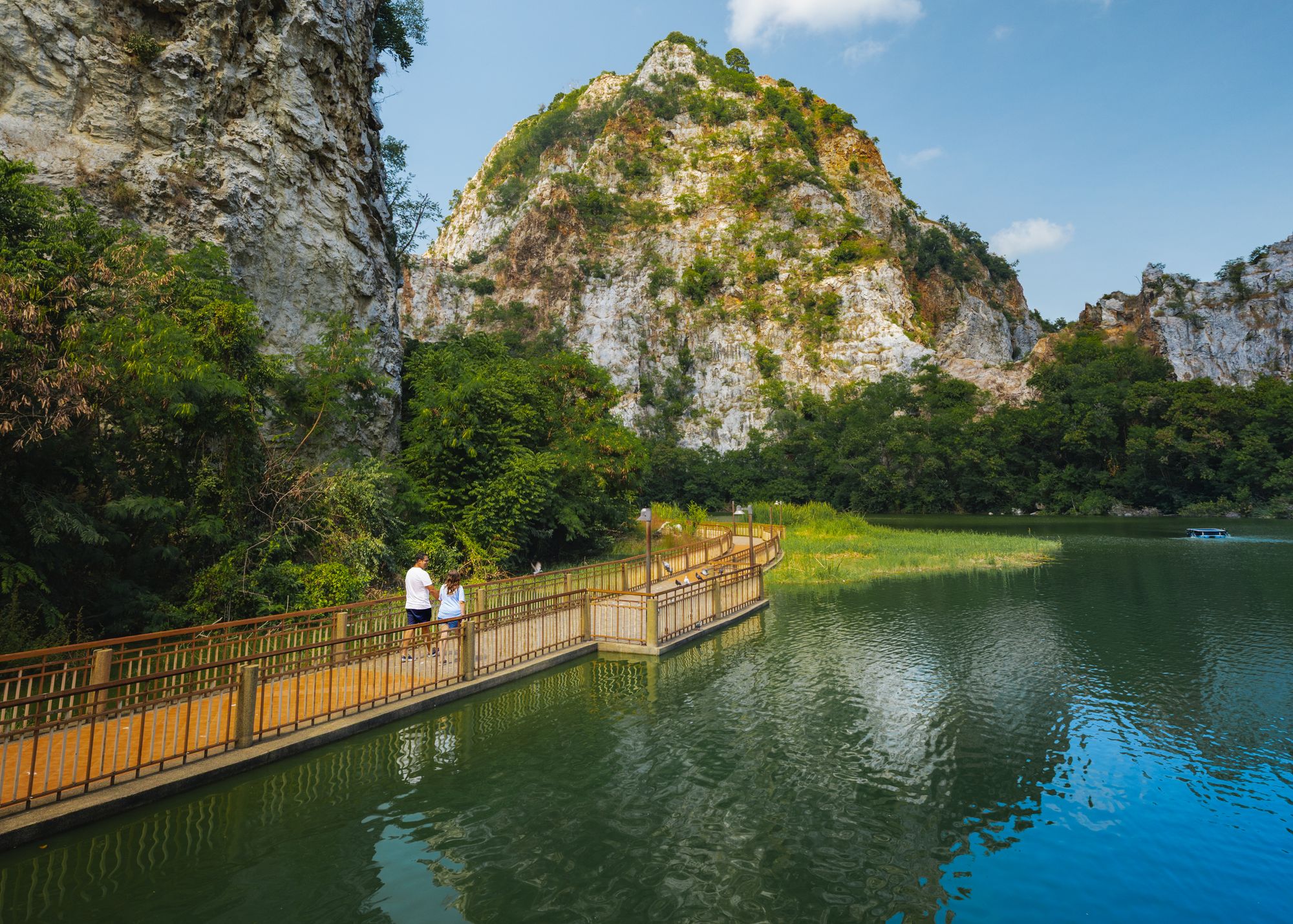 Pao y Andrew caminando por una pasarela junto al lago y las montañas de Khao Ngu Stone Park.